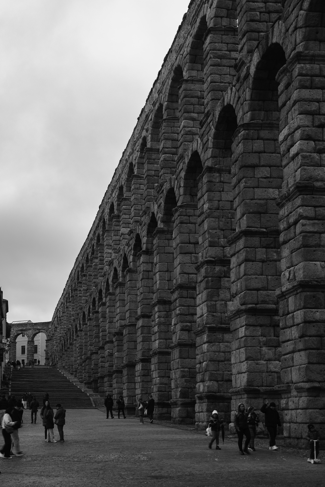 Imposing perspective view of the ancient Roman stone Aqueduct of Segovia, a historic monument in Segovia, Spain, with people walking beneath the granite arches. (c) pmartinasi