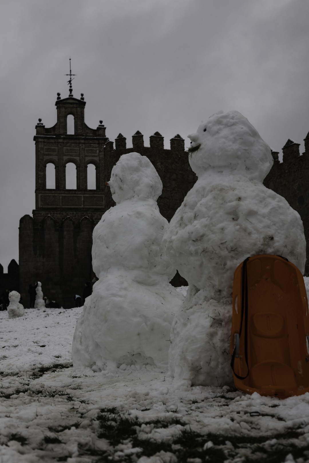 A lively winter scene at the northern stone fortifications of Avila, Spain, where locals and visitors play in the deep snow and build snowmen against the backdrop of the historic medieval walls. (c) pmartinasi