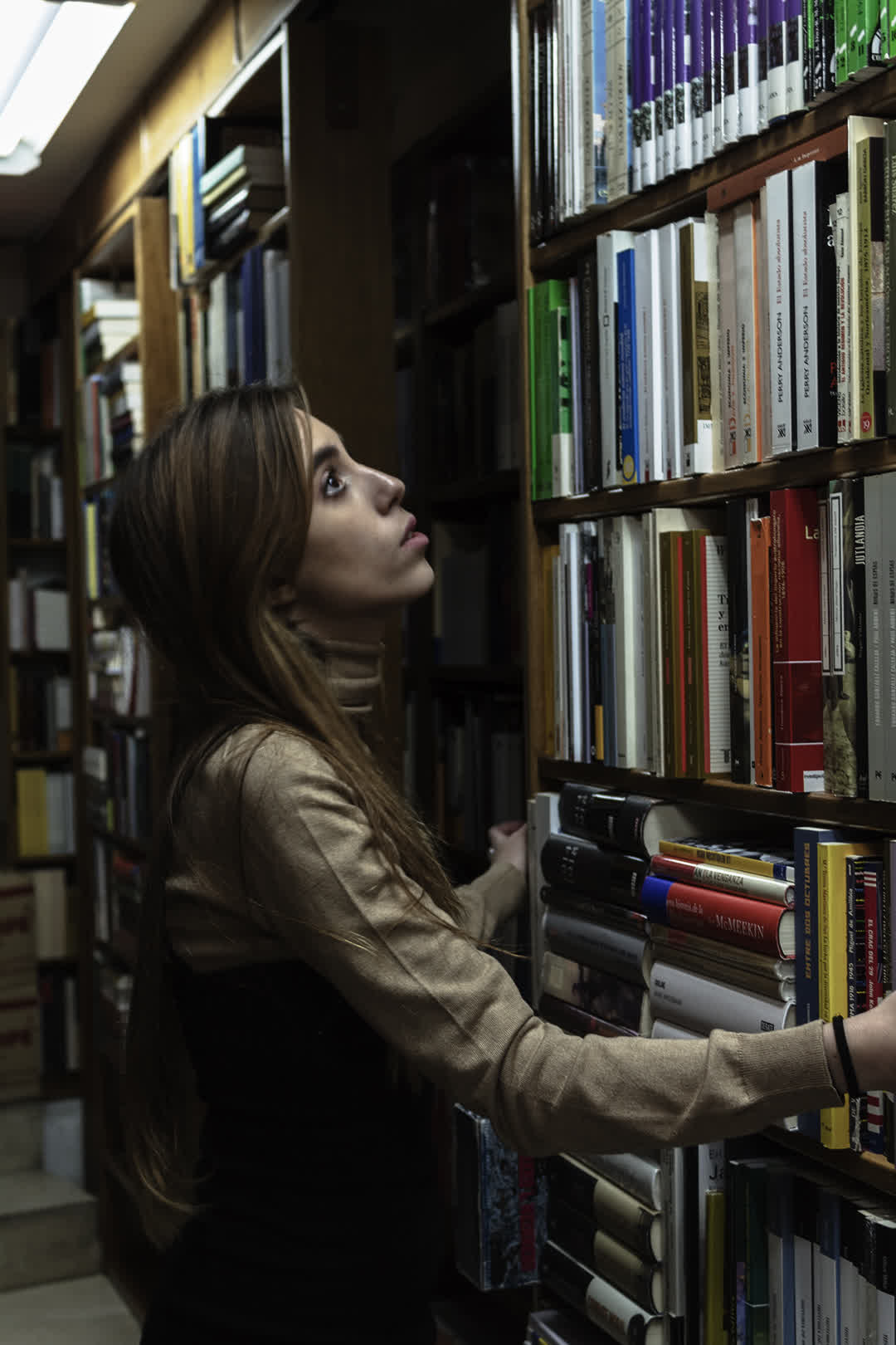Young Woman Browsing Bookshelves in a Cozy Bookshop. (c) pmartinasi