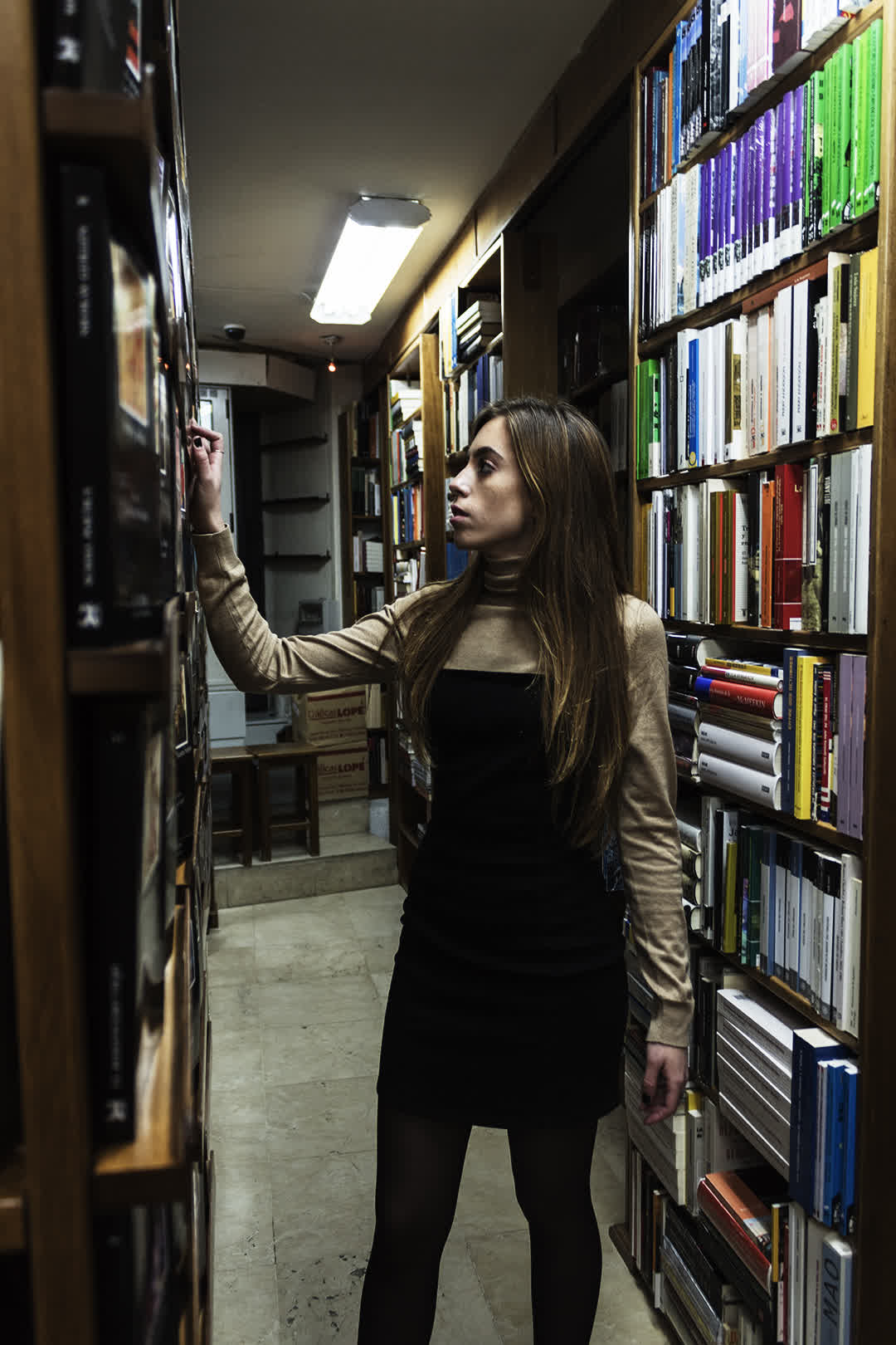 Young Woman Browsing Bookshelves in a Cozy Bookshop. (c) pmartinasi
