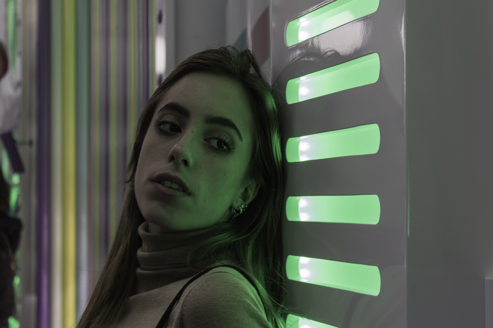 Woman Leaning Against Illuminated Wall with Green Lights in Modern Art Installation. (c) pmartinasi