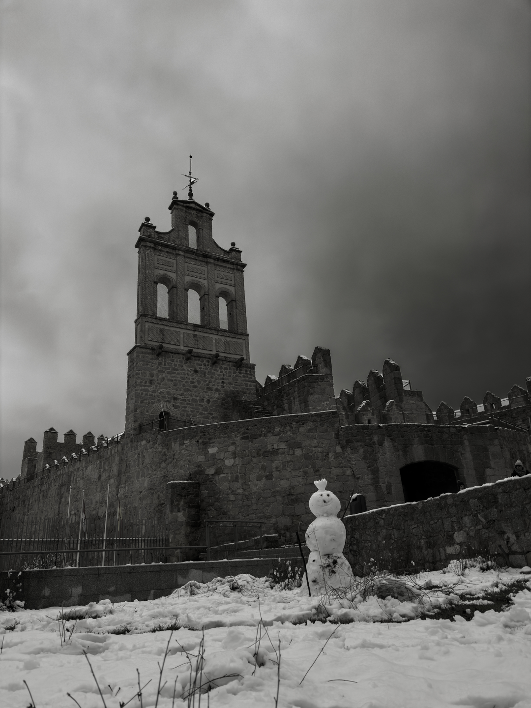 A snowman built in front of the historic Arco del Carmen gateway and the medieval stone rampart walls of Avila, Castile and Leon, Spain, during a cold and snowy winter day. (c) pmartinasi