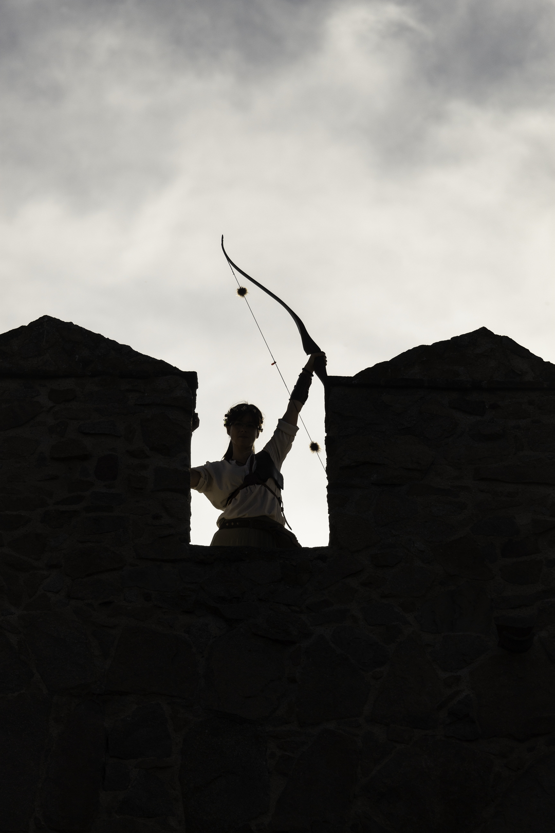  Woman archer raising her bow on the historic rampart walls of Ávila during the Medieval Fair and Market, evoking heritage and tradition. . Medieval Market and Fair at Avila, Spain. September 2025. (c) pmartinasi