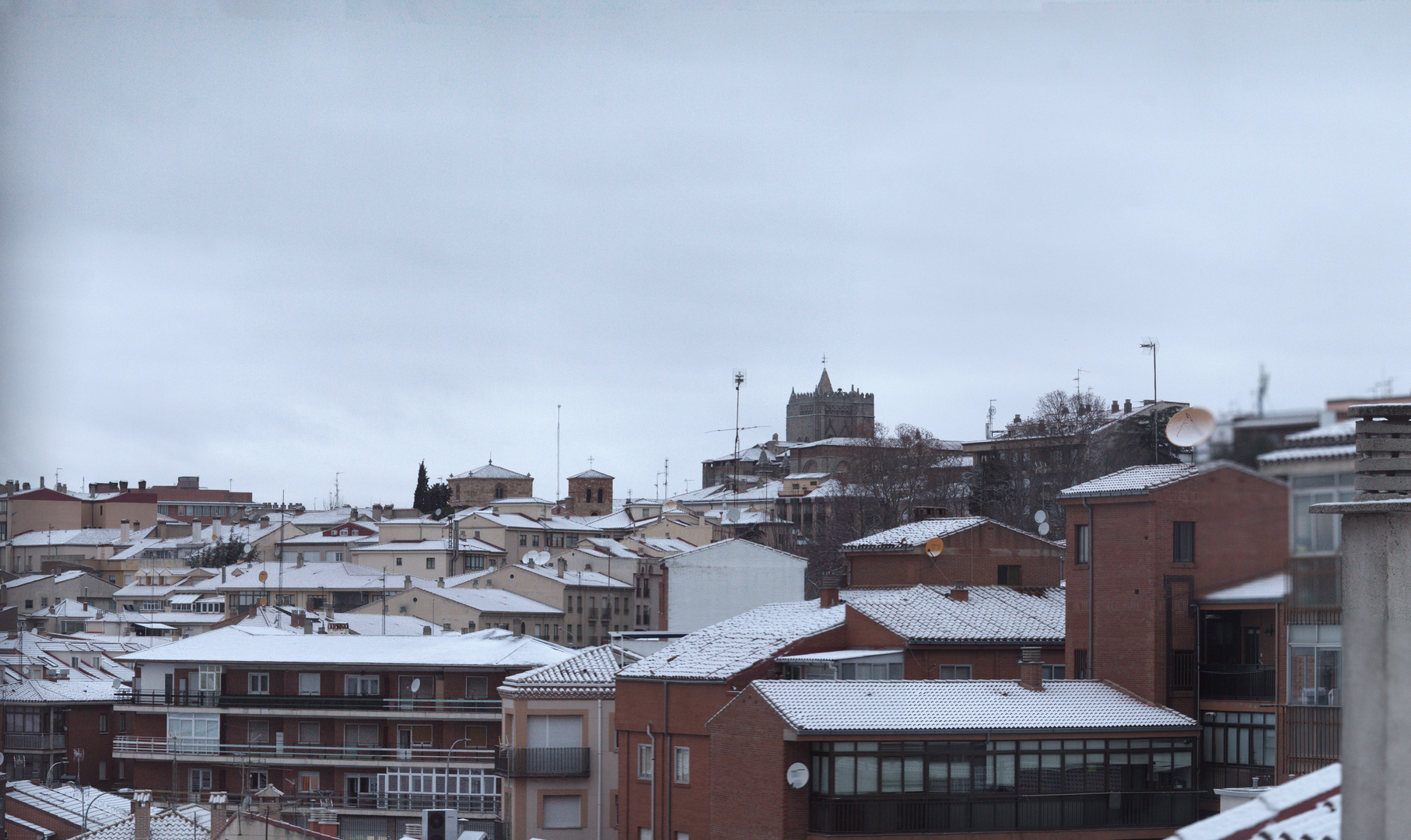 Panoramic winter view of Ávila from the south west, showing snow-covered rooftops, historic church towers and residential buildings, capturing the calm atmosphere of a cold day in a traditional Spanish city. January 2026. (c) pmartinasi