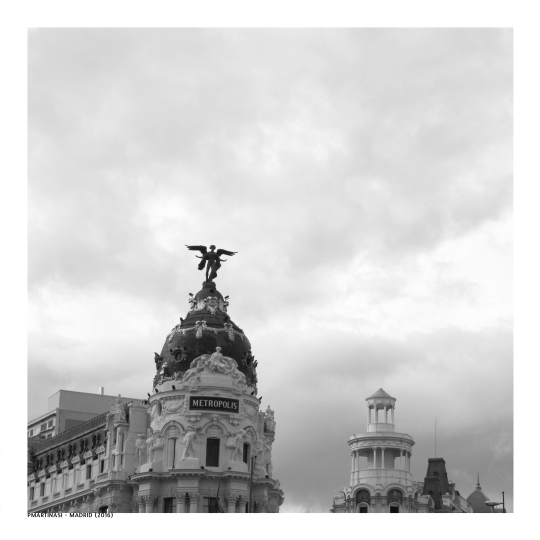  Black and white image of the iconic Metropolis Building on Gran Vía in Madrid, Spain, featuring ornate Beaux-Arts architecture with the famous winged statue against a moody sky backdrop. (c) pmartinasi