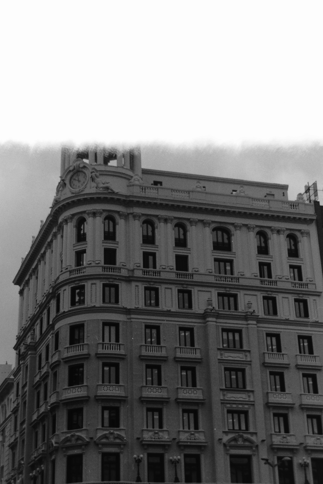Atmospheric monochrome photograph of a grand classical building in Madrid, featuring ornate facades, arched windows, balconies, and a decorative clock tower—capturing the city’s historic charm and cultural heritage. (c) pmartinasi