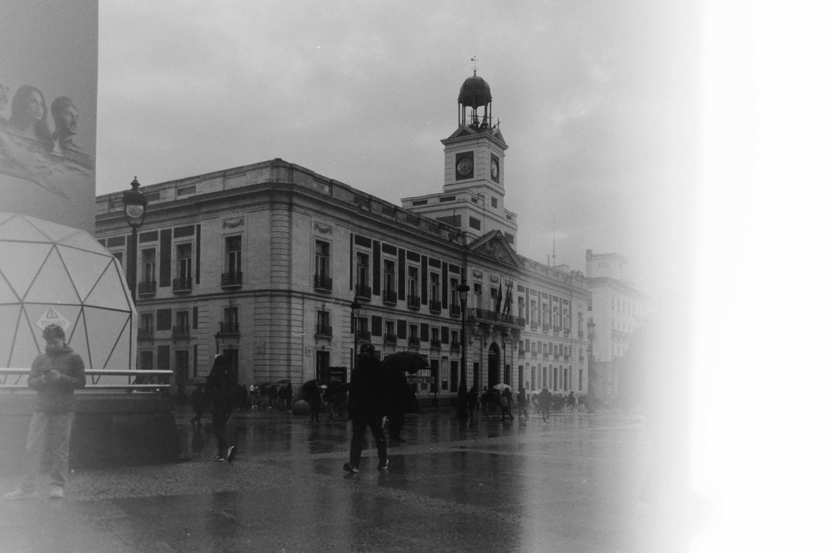 Moody Black and White Rainy Day at Puerta del Sol with Historic Clock Tower and Urban Life (c) pmartinasi