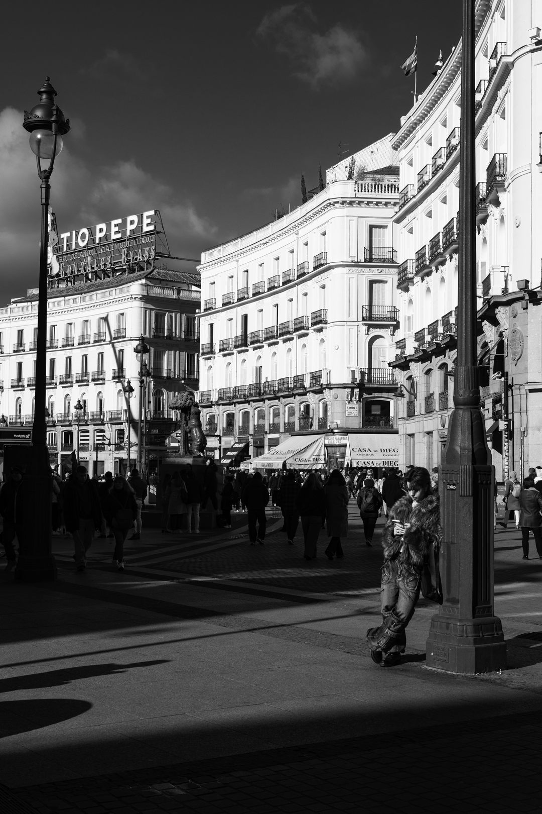 Candid street scene at Puerta del Sol shows people moving through Madrid's most iconic square, framed by elegant historic buildings and bright daylight, reflecting the lively atmosphere and everyday culture of the Spanish capital. (c) pmartinasi