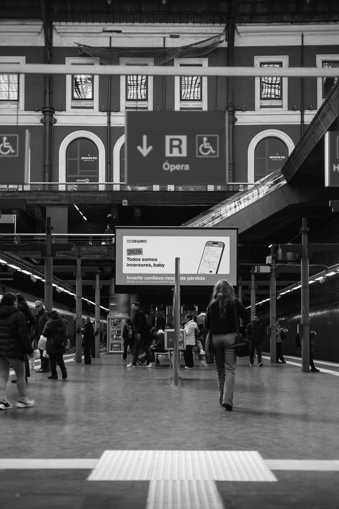 Candid black and white photograph captures a woman in motion blur walking across the platform at the busy Principe Pio Metro Station in Madrid, Spain, Europe. (c) pmartinasi