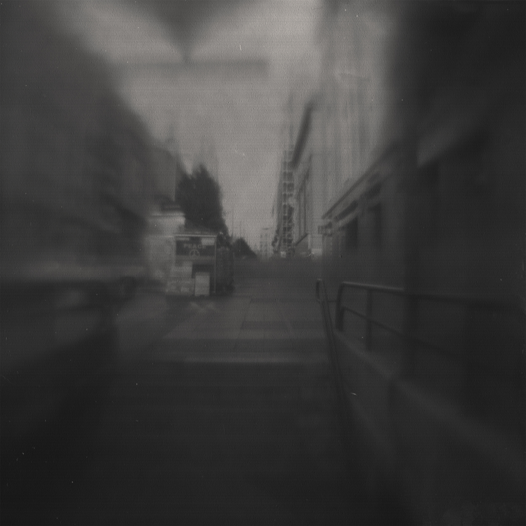 A blurred black-and-white photograph capturing an urban scene near Metro Gran Vía in Madrid. The image evokes a sense of motion and nostalgia, with soft tones and abstract details enhancing its atmospheric quality. Camera design by @joterman. (c) pmartinasi