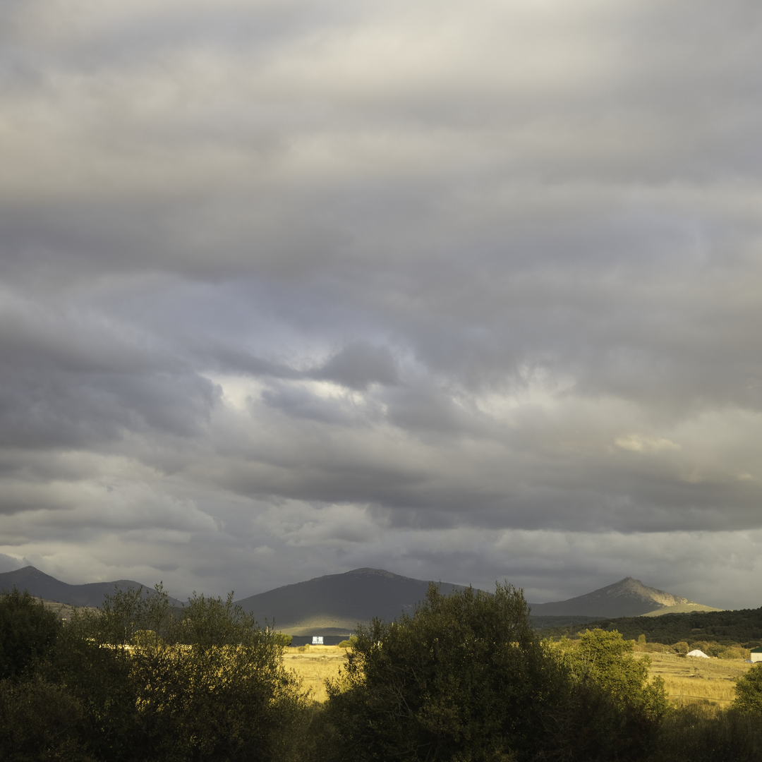  Scenic view of the rural landscape near El Espinar, Segovia, Spain, during autumn. Sunlight pierces through heavy clouds, illuminating the fields and distant mountains in soft golden tones.. October 2025. (c) pmartinasi