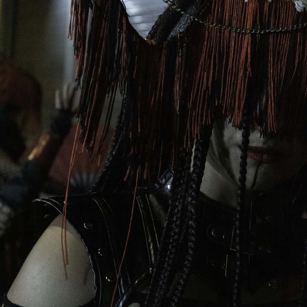  A close-up of a woman in red Asian-inspired costume with braids, fringe mask, and fishnet sleeves, captured while parading at the Medieval Fair and Market of Ávila, Spain. September 2025. (c) pmartinasi
