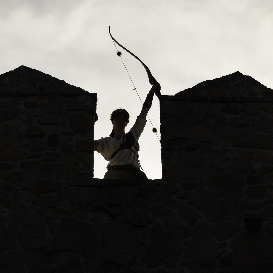  Woman archer raising her bow on the historic rampart walls of Ávila during the Medieval Fair and Market, evoking heritage and tradition. . Medieval Market and Fair at Avila, Spain. September 2025. (c) pmartinasi