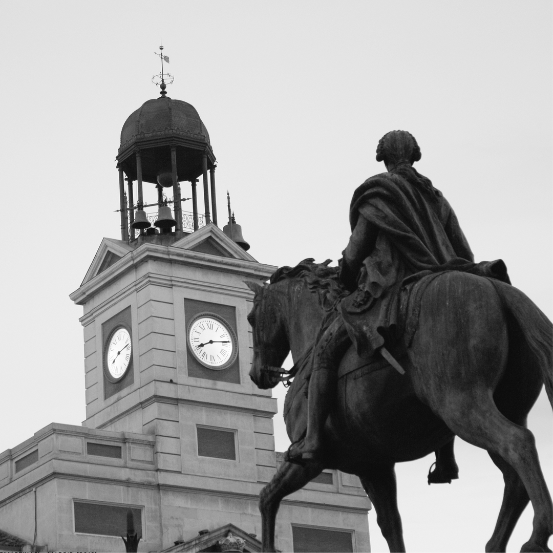  Black and white photograph of the famous Puerta del Sol in Madrid, capturing the equestrian statue of King Charles III and the historic clock tower of the Real Casa de Correos, a central symbol of the city. (c) pmartinasi