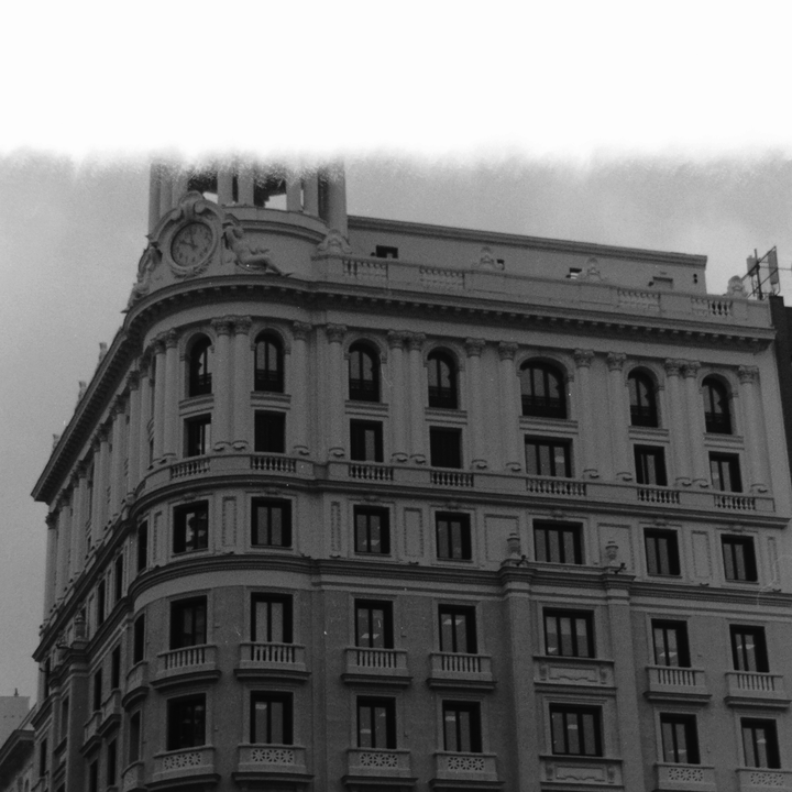 Atmospheric monochrome photograph of a grand classical building in Madrid, featuring ornate facades, arched windows, balconies, and a decorative clock tower—capturing the city’s historic charm and cultural heritage. (c) pmartinasi