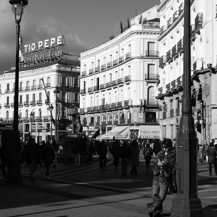 Candid street scene at Puerta del Sol shows people moving through Madrid's most iconic square, framed by elegant historic buildings and bright daylight, reflecting the lively atmosphere and everyday culture of the Spanish capital. (c) pmartinasi