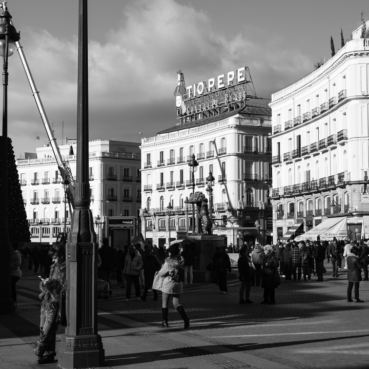 Candid street scene at Puerta del Sol shows people moving through Madrid's most iconic square, framed by elegant historic buildings and bright daylight, reflecting the lively atmosphere and everyday culture of the Spanish capital. (c) pmartinasi
